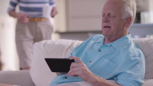 Senior man using tablet computer with woman nearby
