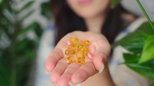 Woman Holding Vitamins with Green Plant Background