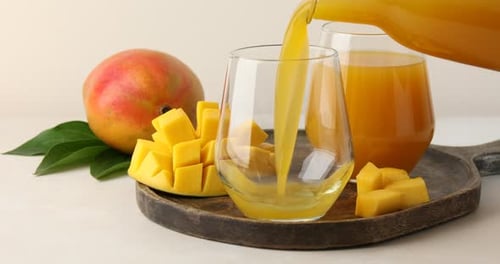 Pouring mango juice into a glass on wooden tray