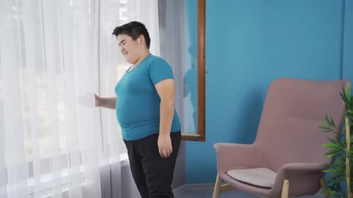 Adipositas-Junge schaut unglücklich vor dem Fenster raus.
