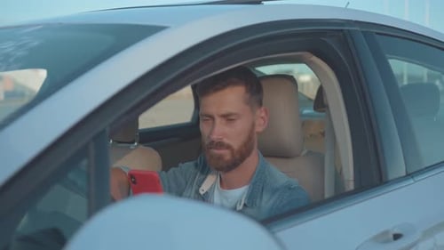 Man Smiling in Car While Using Smartphone