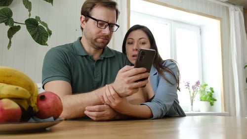 Loving Couple Looking at Phone at Kitchen Table