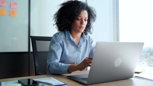 Focused african american businesswoman typing on laptop in modern corporate office