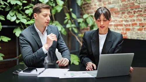Business Colleagues in Formal Wear Discuss a Project at the Office Using Laptop