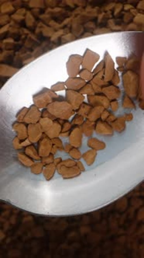 Vertical video. Fingers brushing off soluble coffee granules, top view against the background.
