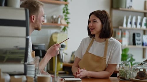 Happy Brunette Girl in a White Tshirt a Cafe Worker Stands Behind the Counter Talking to a Guy