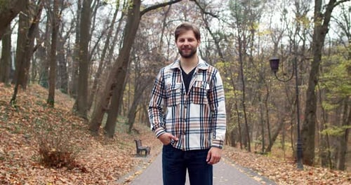Portrait of Successful Stylish Young Man Standing in Park with Trees Leaves in Autumn Looking at