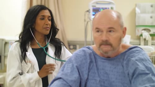 Female doctor listens to patient's heart with a stethoscope bedside in hospital.