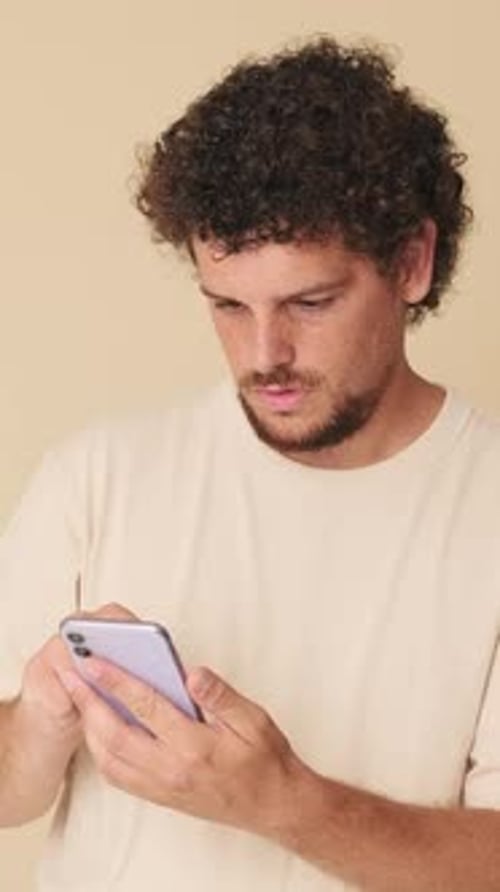 Surprised man with mobile phone in his hands in studio on beige background