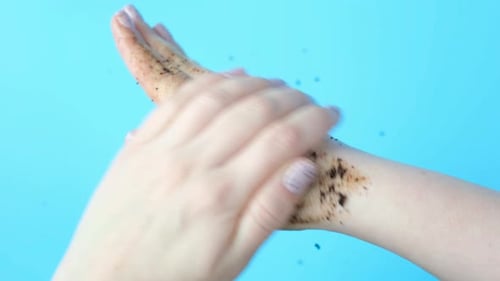 Young woman applies coffee scrub on her hands on blue background, top view.
