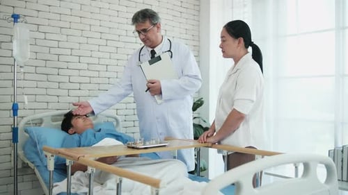 White doctor examines an Asian boy in a hospital ward, consulting with his mum.