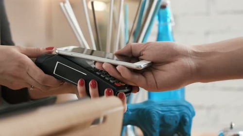 Adult woman working near cash desk as man makes cashless payment in modern restaurant