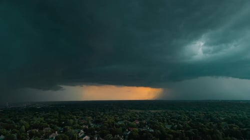 Dunkle Gewitterwolken bewegen sich schnell über einem dunklen, farbenfrohen Abendhorizont über der Stadt. Drohnenweite Sicht