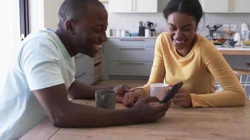 Couple Laughing Together at Smartphone in Kitchen