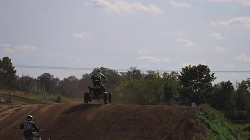 Several quad bikes jump over the hill during race. Tournament and racers going fast over dirt track.