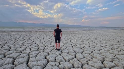 Man Looking at Dried Lake and Cracked Soil