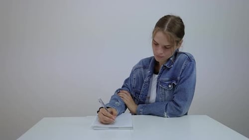 Young Woman Writes in Notebook at White Table