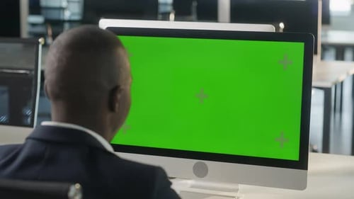 Business African Man Working on Desktop Computer with Green Screen Mock Up Display in Busy Creative