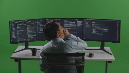 Tired Asian Man Developer Yawning While Write Code With Multiple Computer Screens In Green Screen