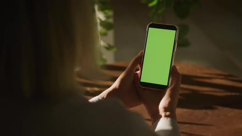 Person Holding Smartphone with Green Screen Indoors