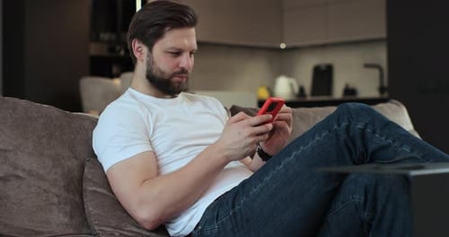 Man Relaxing on Couch with Smartphone Indoors