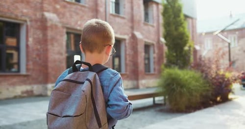 Back view. Schoolboy Little boy child with backpack alone going to school at sunset street outdoors.