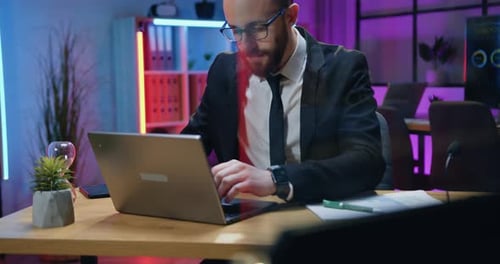 Businessman in formal wear and in glasses working on laptop computer at late time in office sitting