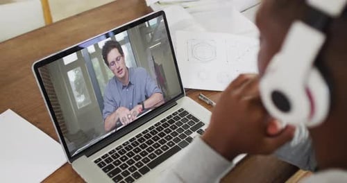 African american male college student wearing headphones having a video call on laptop at home