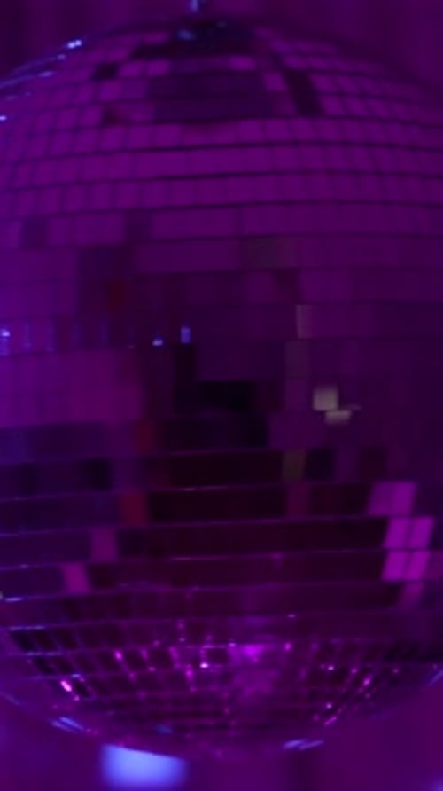 Disco ball spins under colorful lights at late night. Vertical