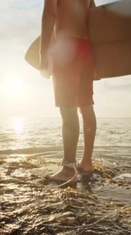 Surfer Standing in the Ocean Holding Surfboard Looking at Sunset