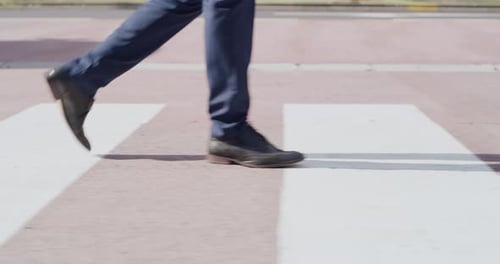 Vista de perto dos pés caminhando sobre uma travessia pública, cruz de zebra e rua urbana em uma cidade ou vila
