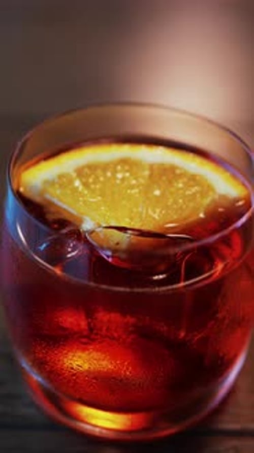 Close up of a Negroni cocktail with orange slice and ice cubes on a wooden table