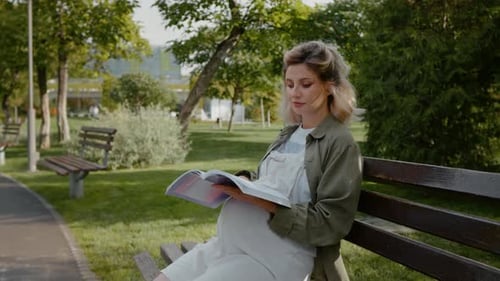 Woman reading books about pregnancy in the park.