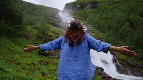 Woman Enjoying Scenic Waterfall View with Open Arms