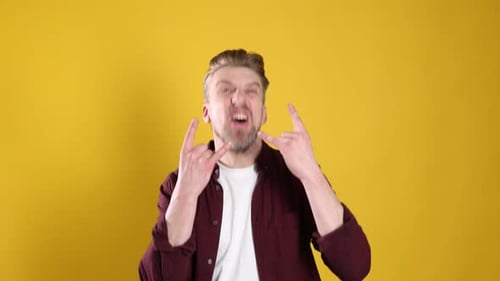 Man showing rock gesture and dancing on yellow background