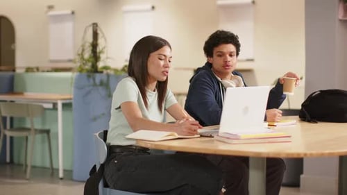 Étudiants discutant de leurs devoirs, prenant des notes et utilisant un ordinateur portable blanc à la table du campus en sirotant un café
