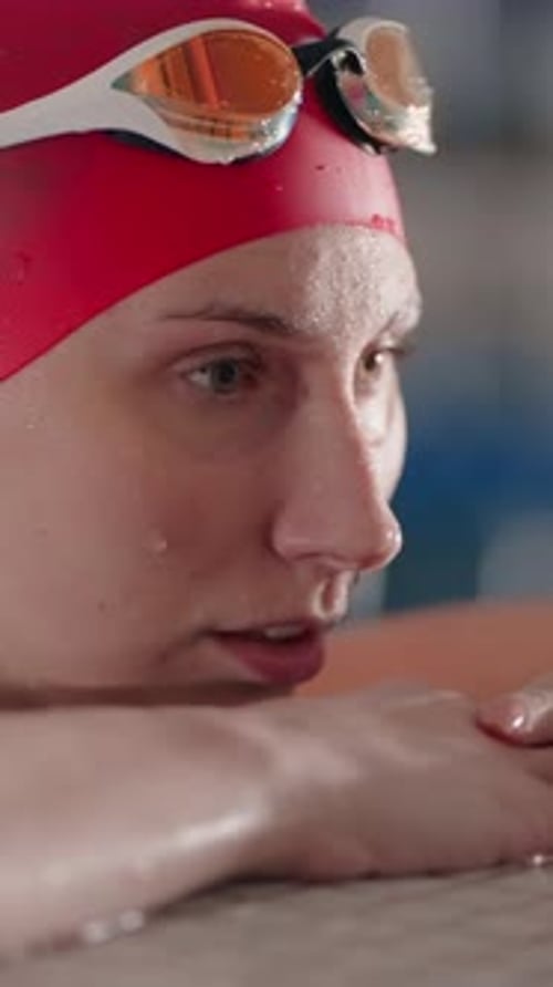 Focused Competitive Swimmer in Red Cap Resting at Pool Edge Water Droplets on Face and Goggles