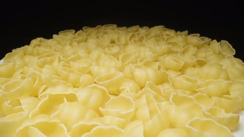 Dry pasta gnocchetti rotates, evenly scattered on a plate, on a black background, close-up. View fro