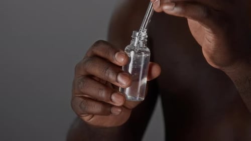 Hand Holds Dropper Bottle, Liquid Drops into Bottle