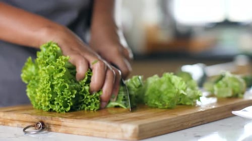 Woman's Hands Chopping the Fresh Green Lettuce on Chopping Board in the Kitchen
