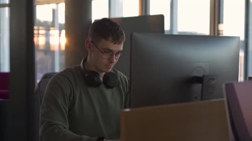 a young manager with a smile works at a computer in his favorite company at sunset