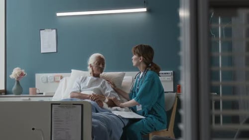 Compassionate Physician Supporting Senior Lady Visiting Her in Hospital Ward