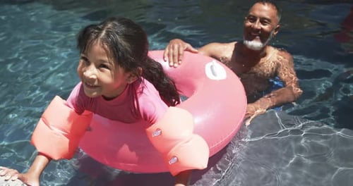 Uma garota birracial com bóias de braço aproveita o tempo na piscina com o avô