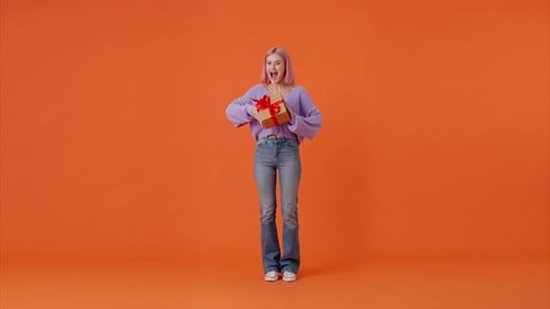 Cheerful Lady Dancing with Gift Box with Red Bow in Studio