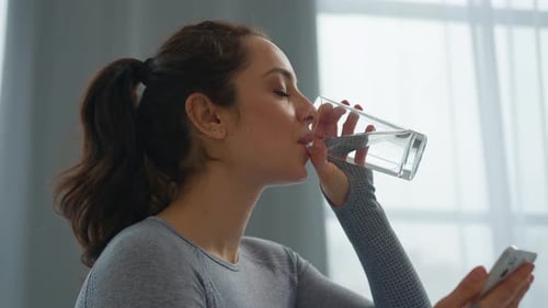 Woman Drinks Water and Uses Phone