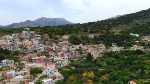 Aerial of a picturesque town on a hill surrounded by forest in Lasithi, Crete