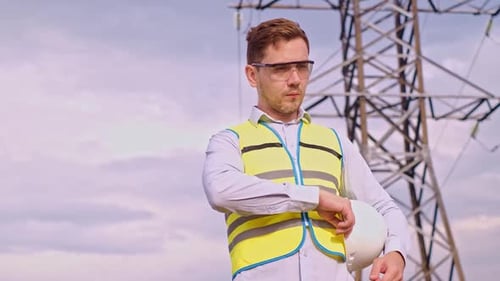 A designer inspects a high voltage tower. An engineer in a hard hat servicing a power transmission p