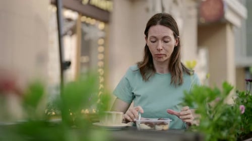 In an Outdoor Cafe a Middleaged Woman Enjoys Dessert and Coffee Immersing Herself in the Atmosphere