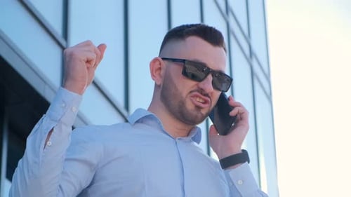 Angry Businessman Arguing While Talking on Smartphone He is Wearing a Blue Shirt