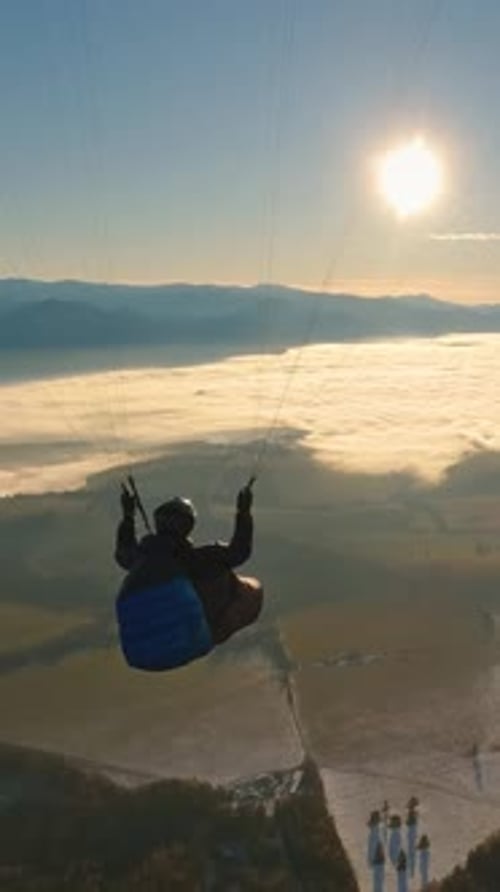 Person paragliding over mountains and clouds during sunset